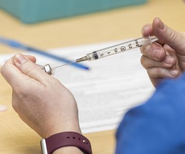 Womans hands wearing a brown watch pulls liquid into a syringe from a small bottle.