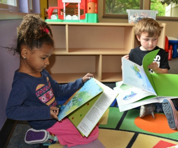 Two toddlers reading large picture books