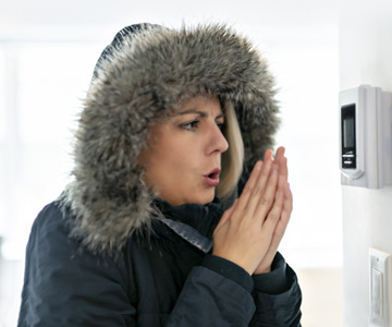 Woman in parka blowing on her hands.