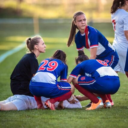 Soccer player injured on the field with players providing aid.