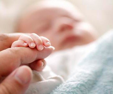 Newborn baby sleeping and hold a parent's finger." (Default Alternate Text: "A newborn's tiny hand holds the hand of her mother.