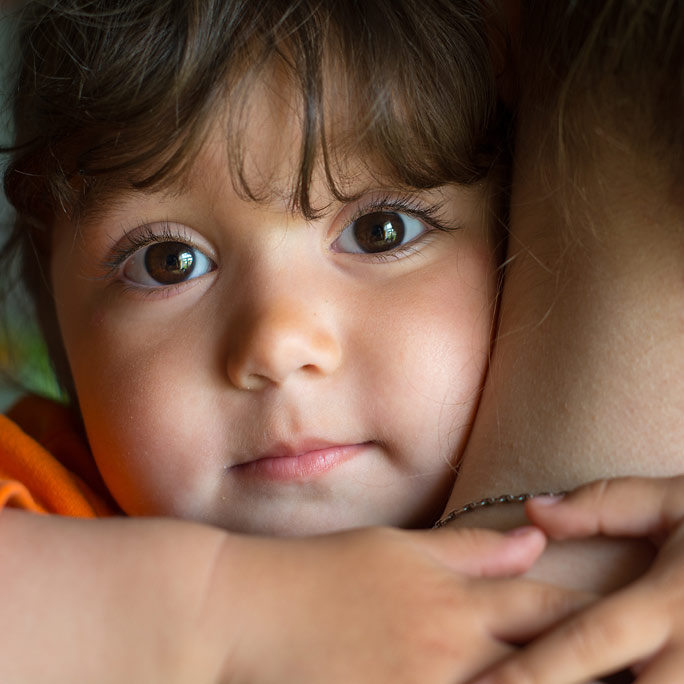 Close up of a toddler with cherub cheeks hugging mom closely.