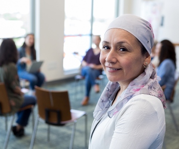 Middle-aged cancer patient looking at the camera a smiling with group of people in a circle of chairs in the background