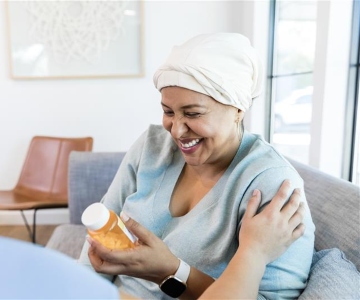 Female cancer patient looking at a bottle of prescription medication and smiling.