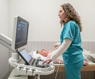 A female nurse performing a chest ultrasound on a senior male patient to screen for an abdominal aortic aneurysm.