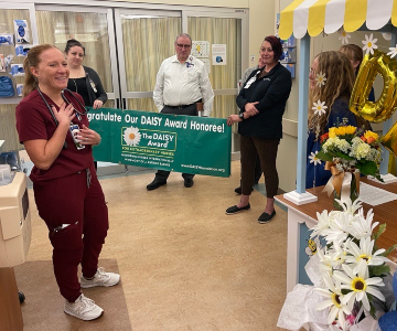 Woman puts her hand near her heart in joy as three people hold a green banner in background