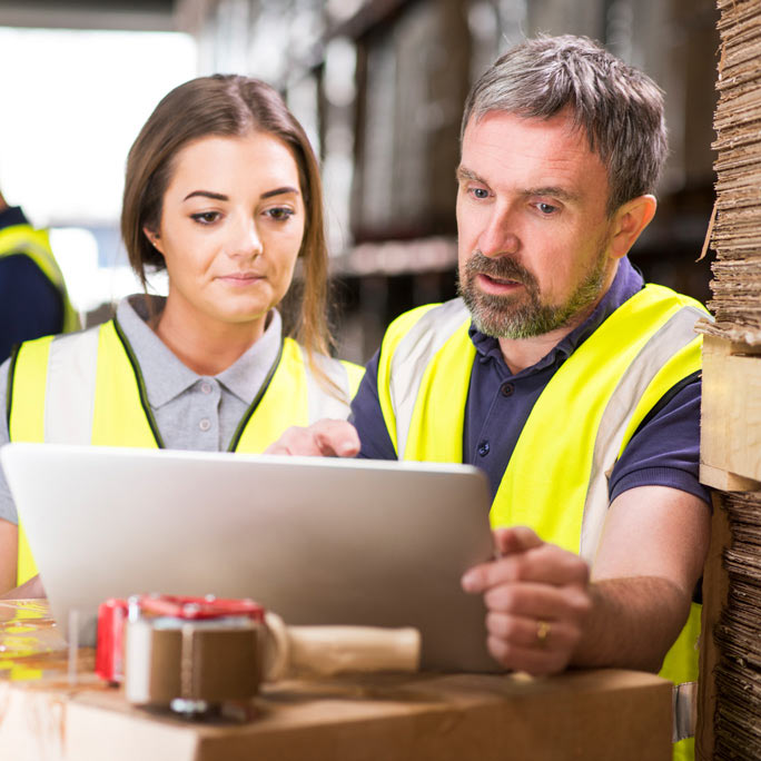 Two safety-vested people focused on a laptop.