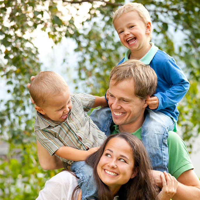 Two laughing children riding smiling parents' shoulders outside.
