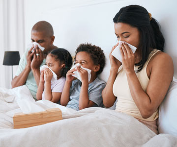 Mother and father with children all in bed and all blowing their noses.