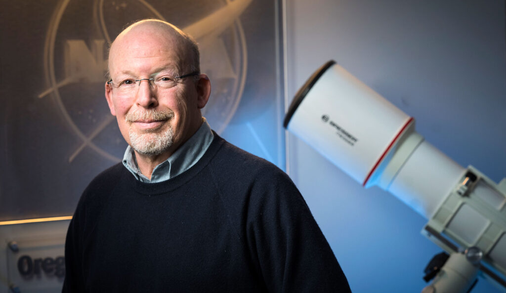Randall smiling with a NASA picture behind him.