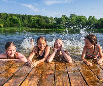 Keep your cool on hot days of summer. Three girls playing in the water by a dock in a lake.