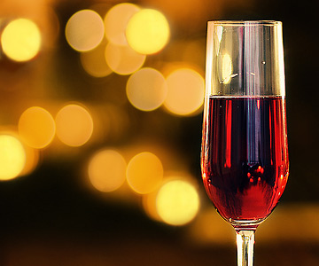A glass or red wine with golden bokeh in the background. The photo has a holiday feel.
