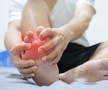 Person holding their foot in pain. An illustrated red light is coming from the pad of the foot, illustrating a gout flare up.