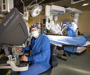 Clinician sitting at screen with robot's arms in background.