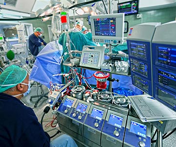 Doctor checks data of cardiopulmonary bypass machine with heart team in background of operating room.