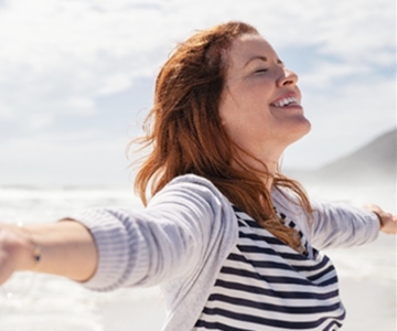 Smiling woman with outstretched arms on the Oregon beach.