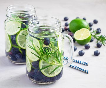 Mason jar of water with blueberries, rosemary sprigs and lime.