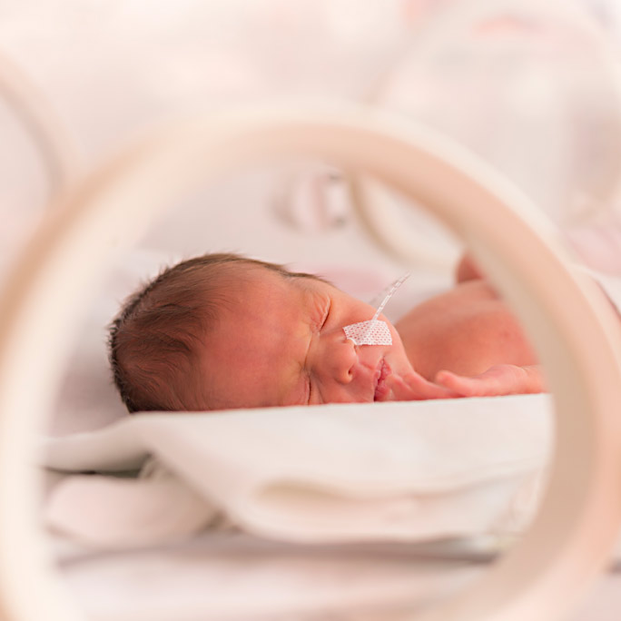 A preemie newborn baby in a incubator with monitoring equipment nearby,