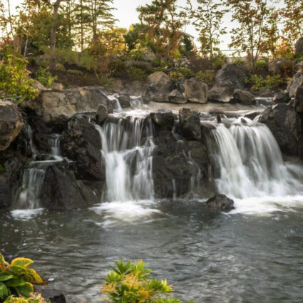 Waterfall rock feature at a healing garden with trees and small shrubs.