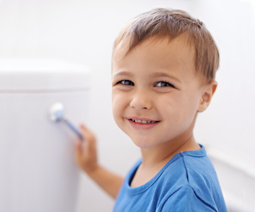 Little boy potty training and flushing a toilet while smiling.