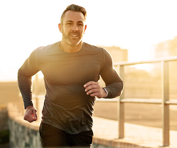 Athletic middle aged man running with sun behind him.