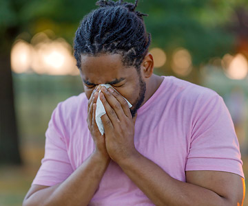 Man on a spring day sneezing into a tissue.