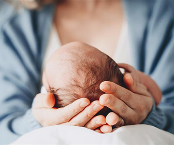 A mother holding her baby in front of her and cradling the baby's head in her hands.