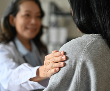 smiling nurse placing a supportive hand on the shoulder of a young woman