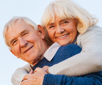 Smiling senior couple, woman with her arms around man's shoulders.