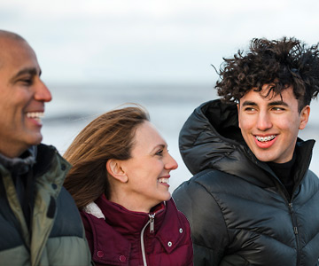 Parents and teenage son walking on beach together wearing coats.