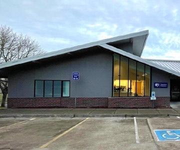 Exterior of a building with bluish grey early morning clouds and an empty parking lot.