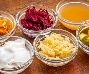 A picture of small bowls containing a variety of probiotic foods, including yogurt, pickled beets, vinegar, pickles and sauerkraut.