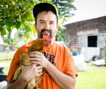 A smiling Anthony holding a chicken.