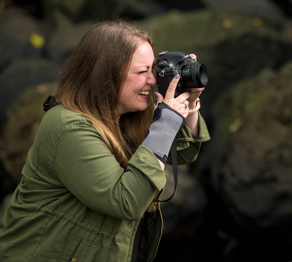 Ashley smiling while peering through her camera's viewfinder and taking a picture.