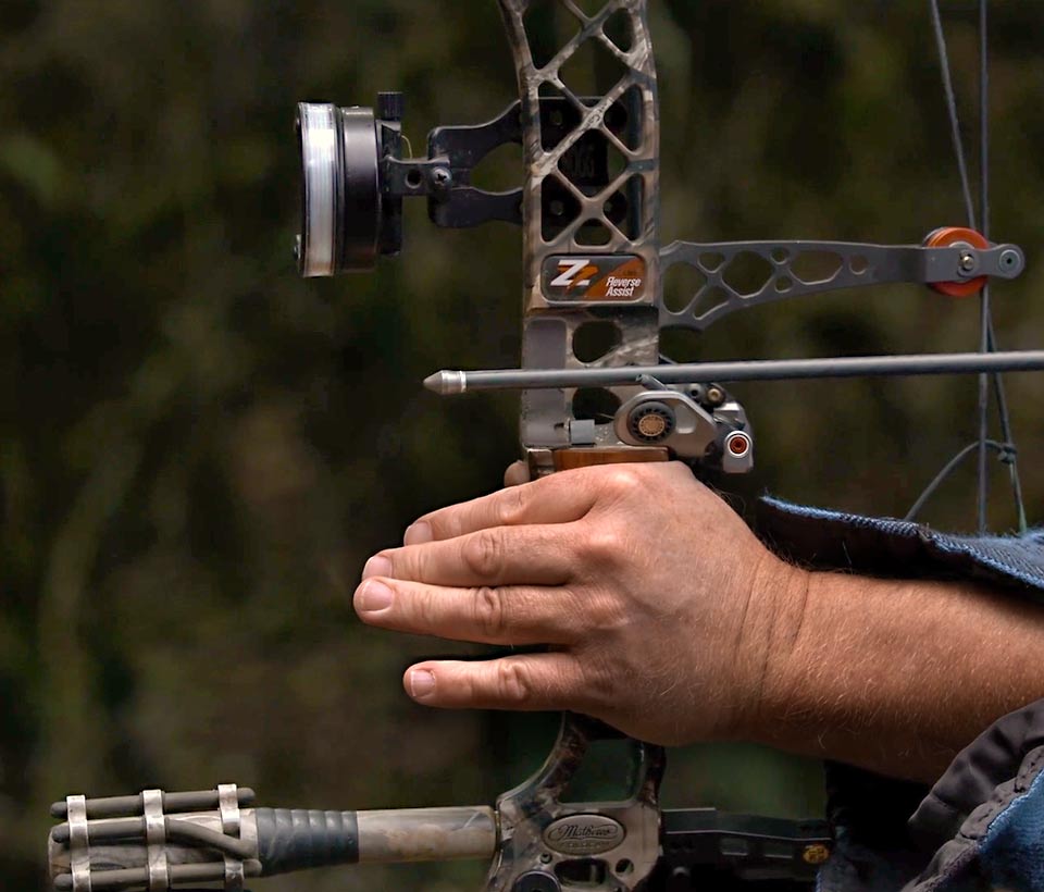 A close up of John's hand holding his bow with the arrow in place.