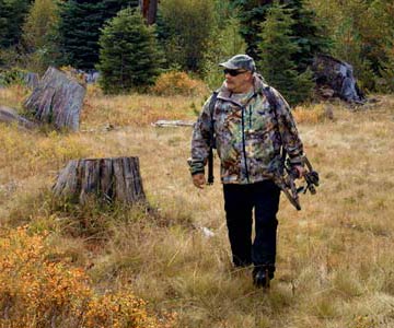 John out in the woods dressed in camouflage and carrying his bow.