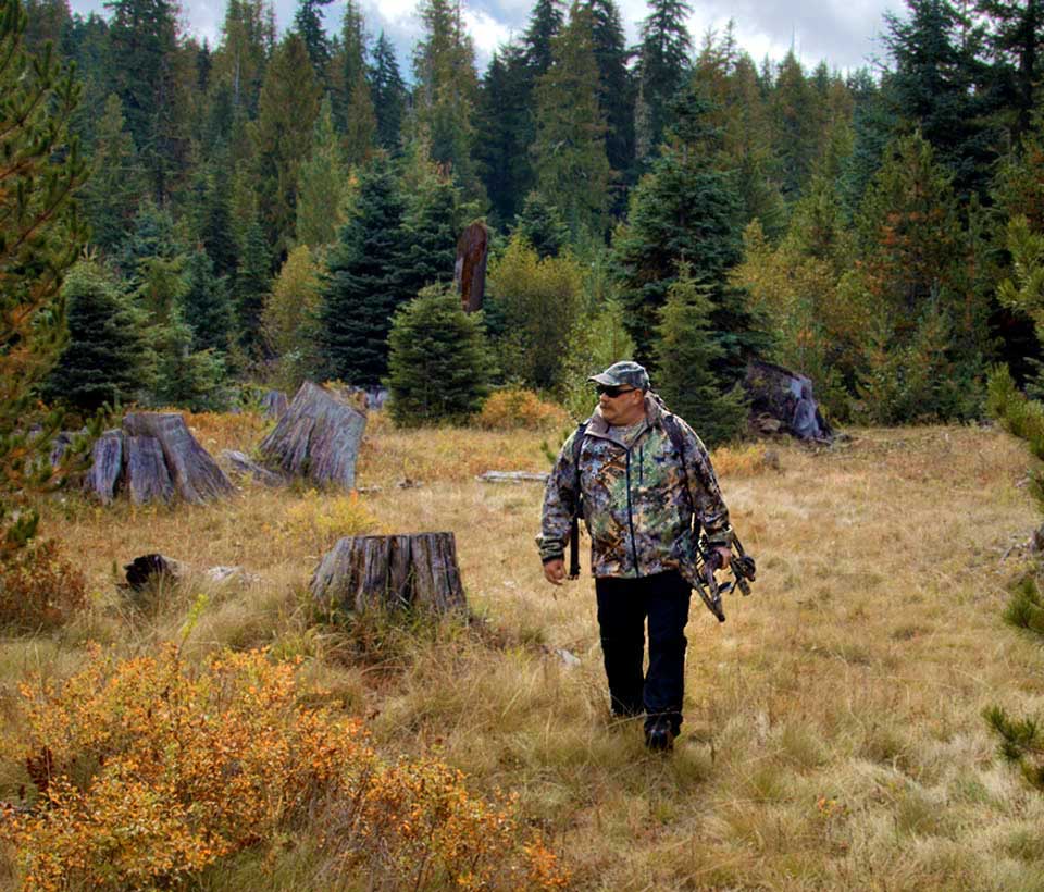 John out in the woods dressed in camouflage and carrying his bow.