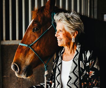 Kathy and her horse both looking outside from inside of the barn.