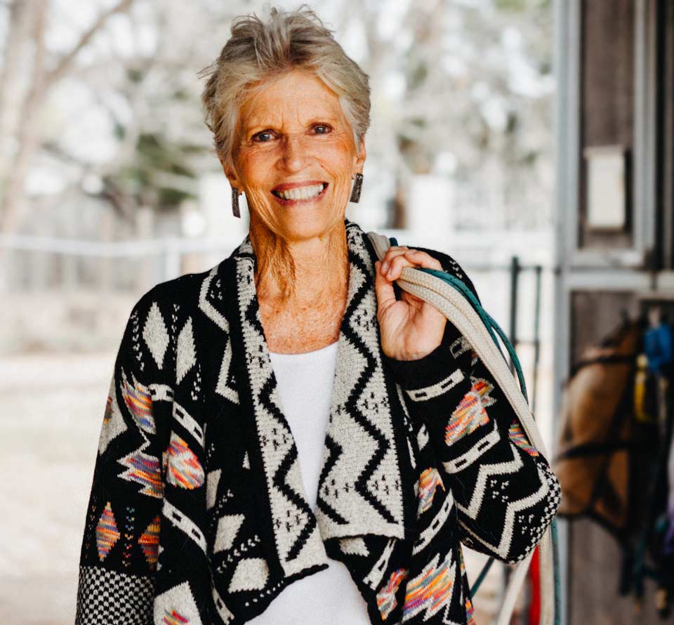 Kathy smiling with horse gear over her shoulder.