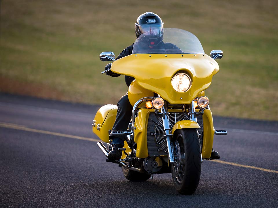 Front view of Kent on his bright yellow motorcycle travelling down a road.
