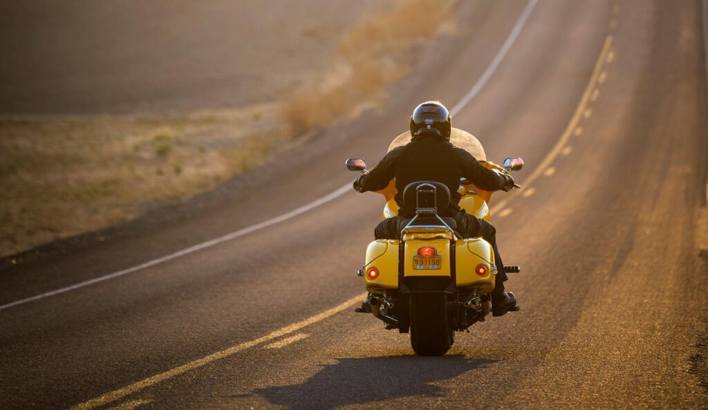 A view from behind as Kent travels down a road on his bright yellow motorcycle.