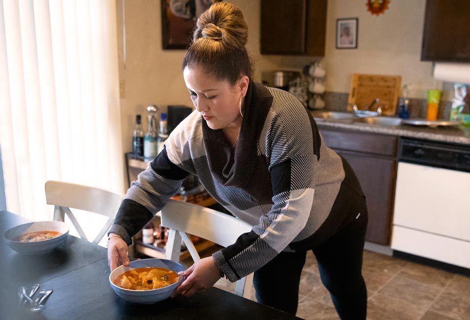 Maria's daughter-in-law placing a bowl of menudo on the dining room table.