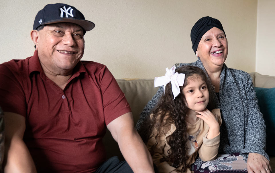 Maria and her husband sitting with grand daughter in their living room.