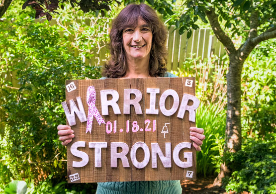 Sonia holding a sign which reads, "Warrior Strong" commemorating her breast cancer survival.