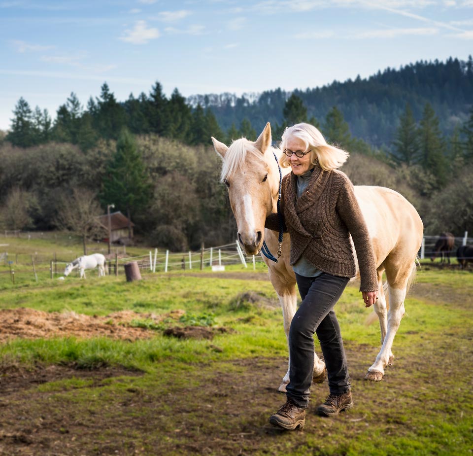 Suzy leading her horse Secret, with the pasture behind them.