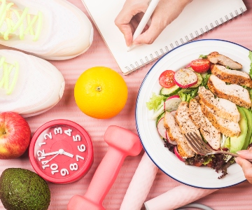 Healthy concept to portray resetting your routines with nutrition food in lunch box and fitness equipment with woman writing time to get healthy on diary book.
