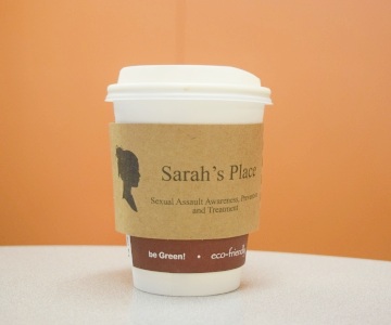 A Sarah's place coffee sleeve on a cup of coffee.