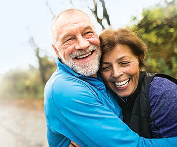 A laughing couple standing outdoors in an embrace.