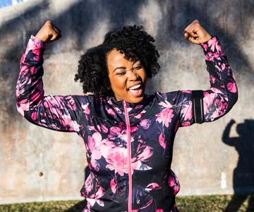 Woman in a pink camo running attire flexes in the sunshine.