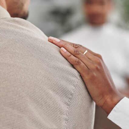 Close up of a woman's supportive hand on man's shoulder.